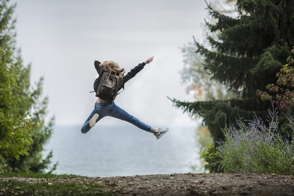 femme de dos avec un sac à dos sautant de joie